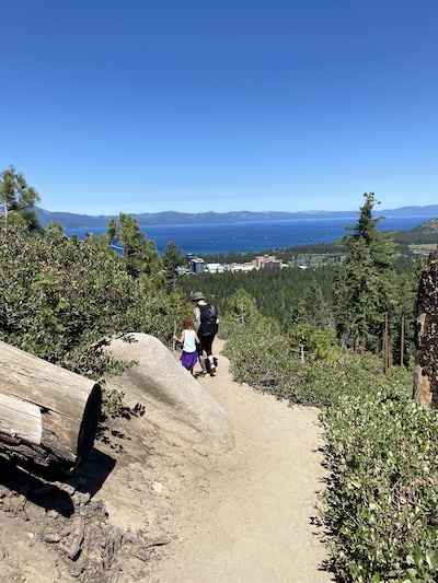 summer activities Lake Tahoe photo of man and child hiking on trail above a blue lake